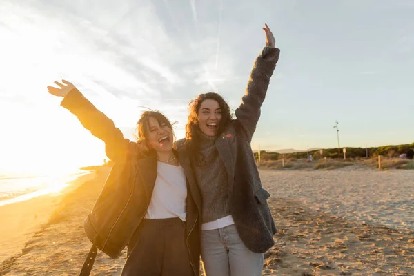 Excited friends raising hands on sandy beach in Barcelona — Stock Photo