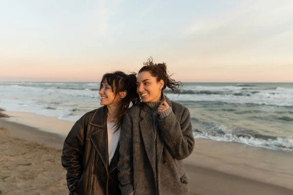 Улыбающиеся молодые женщины смотрят в сторону, стоя на пляже в Испании — стоковое фото