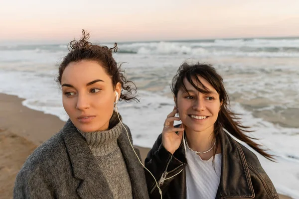 Mujer sonriente usando auriculares con cable con un amigo en la playa de Barcelona - foto de stock