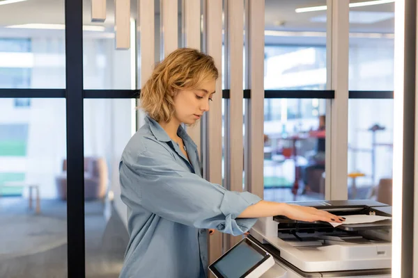 Young blonde woman with wavy hair using modern printer in office — Photo de stock