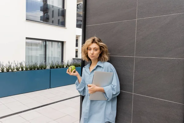 Giovane donna con capelli ondulati in possesso di mela verde e laptop vicino all'edificio dell'hotel a Barcellona — Foto stock