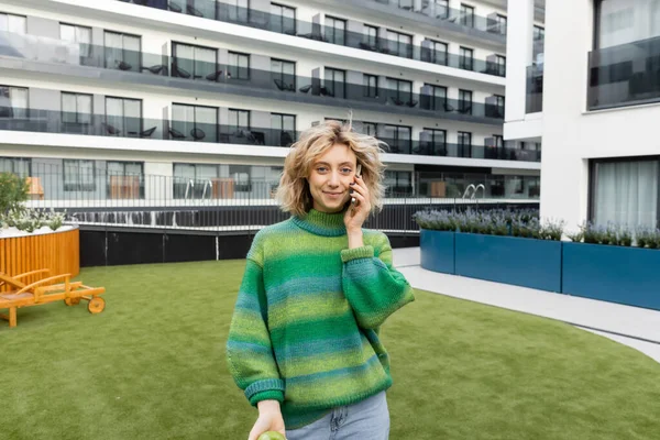 Allegra giovane donna in maglione verde che parla su smartphone vicino all'edificio dell'hotel a Barcellona — Foto stock