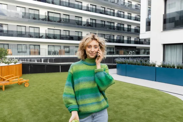 Alegre joven en jersey verde hablando en smartphone cerca del edificio del hotel en Barcelona - foto de stock