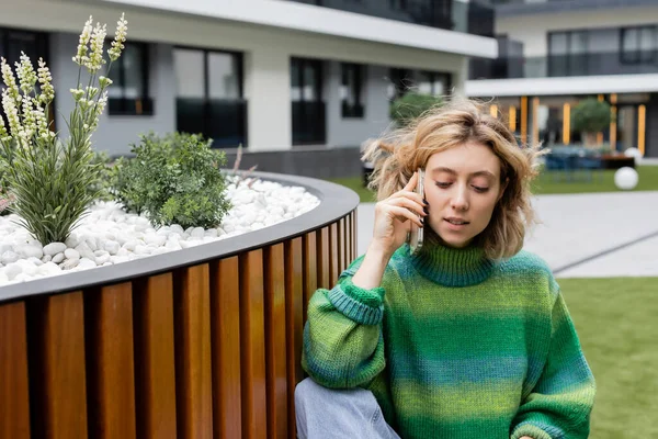 Giovane donna bionda in maglione verde che parla su smartphone vicino all'edificio dell'hotel a Barcellona — Foto stock