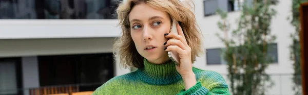 Mujer joven en jersey hablando por teléfono inteligente cerca del hotel en Barcelona, pancarta - foto de stock