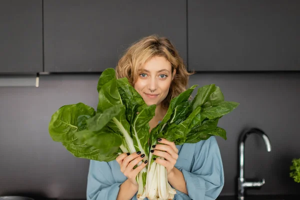 Trafitto giovane donna sorridente e tenendo foglie di cavolo verde in cucina — Foto stock