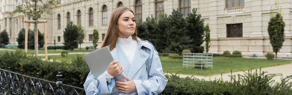 Молода жінка в синьому плащі тримає ноутбук біля історичного будинку у Відні. — стокове фото