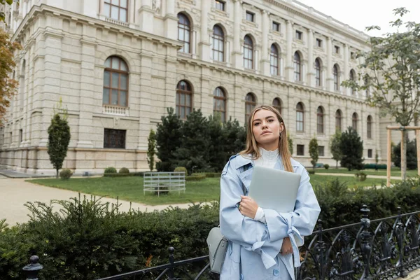 Pretty woman in blue trench coat holding laptop near historical building in Vienna — Stock Photo
