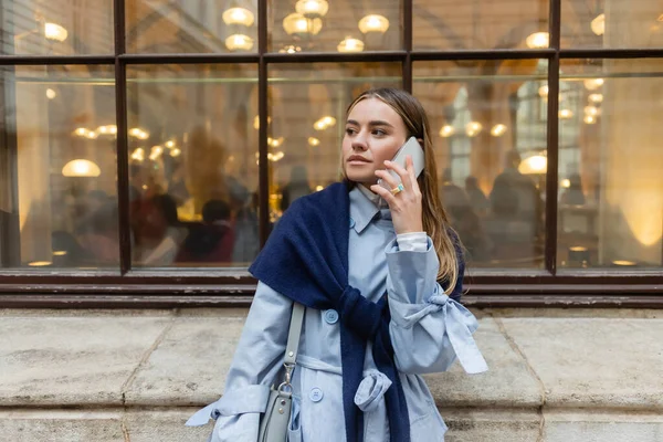 Stylish woman with scarf on top of blue trench coat talking on smartphone on street in Vienna — Stock Photo