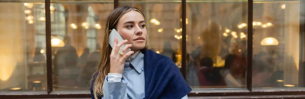 Стильная женщина с шарфом на верхней части голубой куртки разговаривает по смартфону на улице в Вене, баннер — стоковое фото