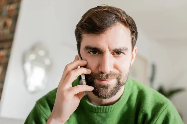 Ritratto di uomo bruna e barbuto in maglione verde che parla su smartphone e guarda la macchina fotografica — Foto stock