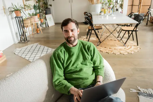 Freelancer alegre e barbudo em green jumper usando laptop e desviando o olhar, trabalho remoto — Fotografia de Stock