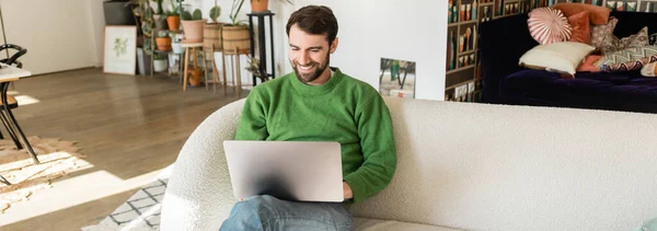 Feliz morena y freelancer barbudo en jersey verde y jeans trabajando en laptop, banner - foto de stock