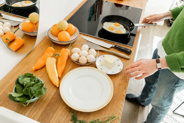 Vue recadrée de l'homme cuisinant des œufs près du beurre, des poivrons et des épinards sur le plan de travail dans la cuisine moderne — Photo de stock