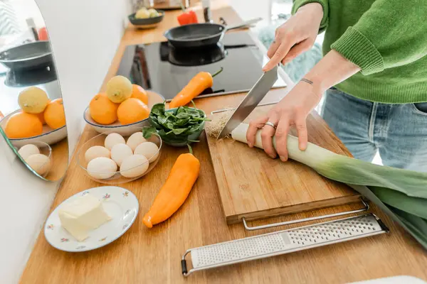 Cropped tattooed man cutting fresh leek near eggs, butter and food on worktop in modern kitchen — Stock Photo