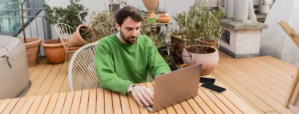 Pigiste dans écouteur à l'aide d'un ordinateur portable et de travailler sur le toit-terrasse de la maison, bannière — Photo de stock