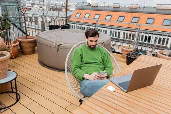 Indépendant barbu travaillant près d'un ordinateur portable sur la table sur le toit-terrasse de la maison à Vienne, Autriche — Photo de stock