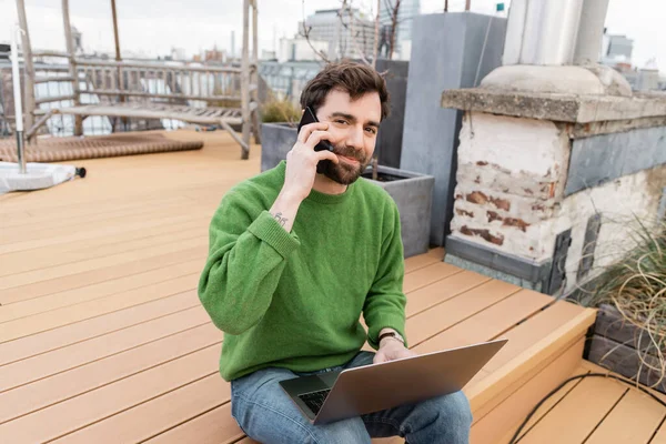 Uomo barbuto parlare su smartphone e lavorare sul computer portatile sulla terrazza panoramica a Vienna, Austria — Foto stock