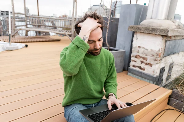 Freelancer tocando el cabello y usando laptop en la terraza de la azotea en Viena, Austria - foto de stock