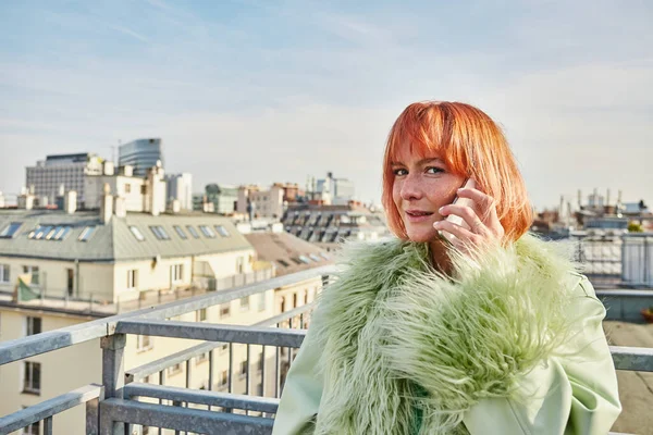 Positive Trendfrau spricht auf Smartphone und blickt auf Dachterrasse in Wien in die Kamera — Stockfoto