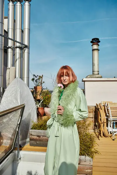 Trendfrau in stylischer Kleidung hält Blumen in die Kamera auf der Dachterrasse in Wien — Stockfoto