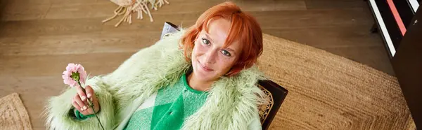 Mulher alegre em outerwear elegante segurando flor em poltrona no apartamento moderno em Viena, banner — Fotografia de Stock