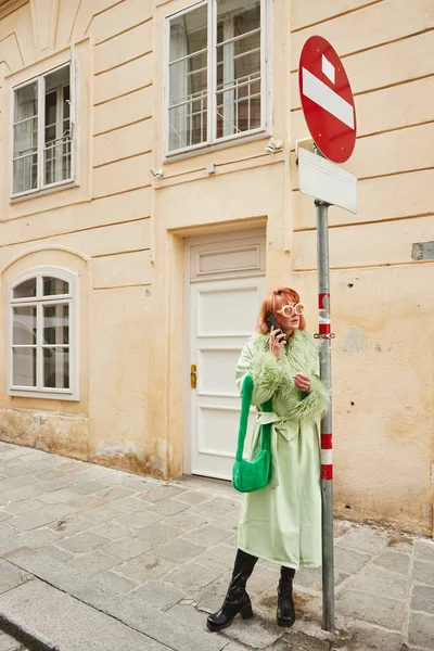 Mujer de moda en gafas de sol y atuendo casual hablando en el teléfono inteligente en la calle urbana de Viena - foto de stock