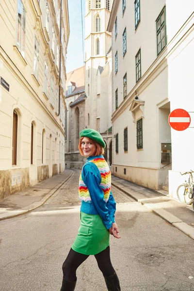 Mujer alegre en boina y ropa elegante mirando a la cámara en la calle de la ciudad en Viena, Austria - foto de stock