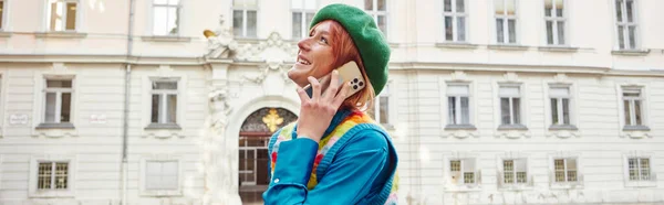 Сучасний спосіб життя, радісна жінка в барвистому жилеті розмовляє на смартфоні на вулиці у Відні, банер — стокове фото