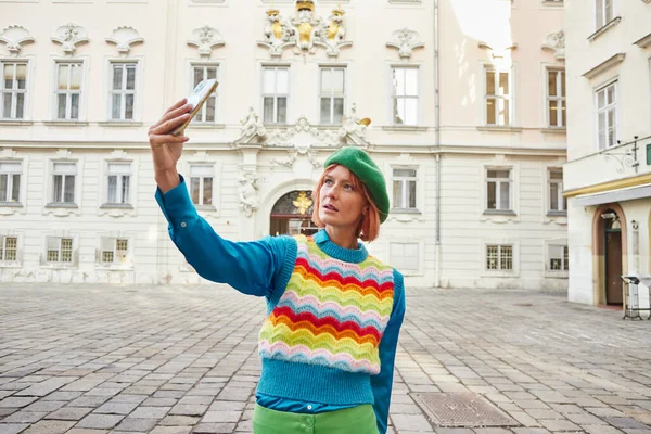 Mulher na moda em colete colorido e boina tomando selfie no smartphone na rua em Viena — Fotografia de Stock