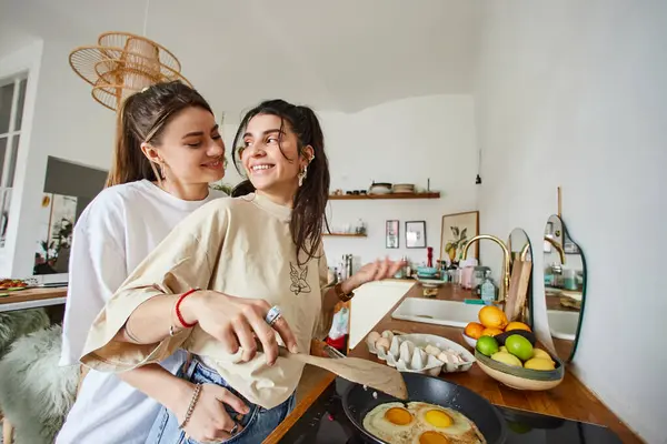Happy and young lesbian couple in 20s cooking breakfast together, intimate moment in kitchen — Stock Photo