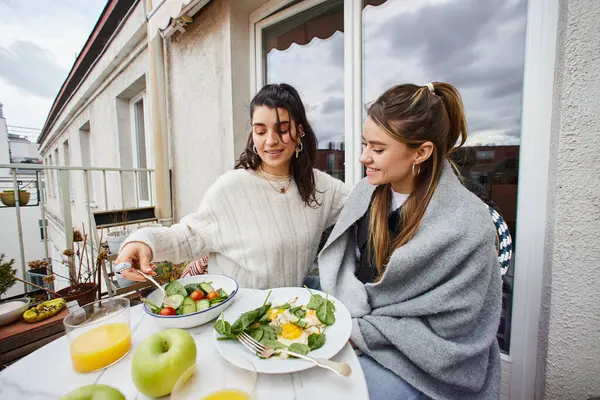 Feliz y joven pareja de lesbianas disfrutando de un desayuno saludable en el balcón en casa, lgbt amor - foto de stock
