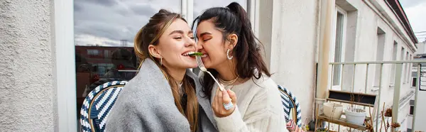 Smiling lesbian woman feeding her girlfriend while having breakfast on balcony, lgbt couple banner — Stock Photo