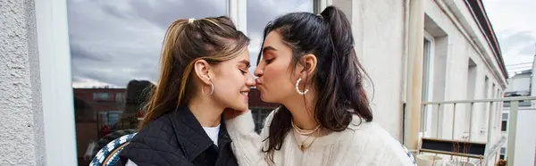 Young lesbian woman kissing nose of her girlfriend while sitting together on balcony, lgbt banner — Stock Photo