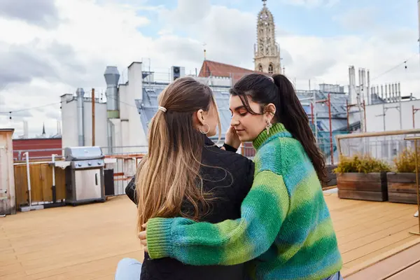 Tender moment between young lesbian women sitting together on a rooftop, cityscape backdrop — Stock Photo
