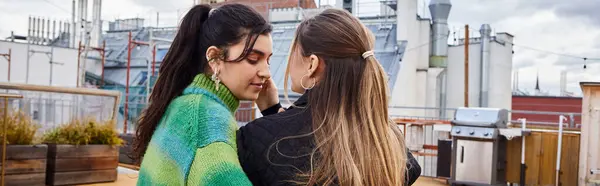 Pancarta de tierno momento entre jóvenes lesbianas sentadas juntas en una azotea, paisaje urbano - foto de stock