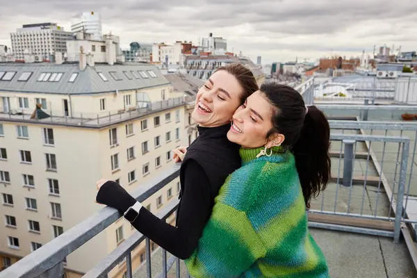 Happy lesbian couple in casual attire looking at city on rooftop, a moment of love and connection — Stock Photo