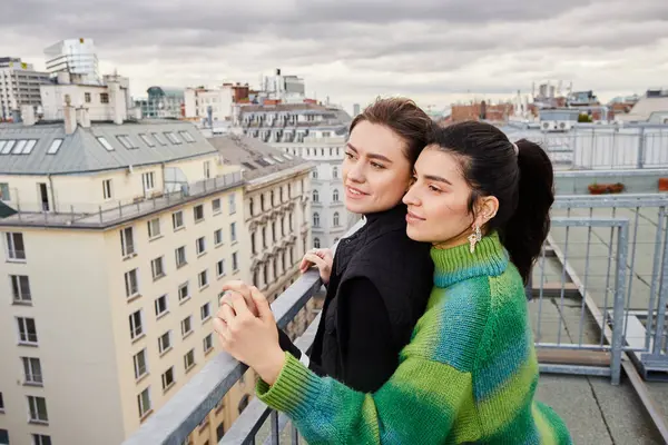 Joyful lesbian couple in casual attire looking at city on rooftop, a moment of love and connection — Stock Photo