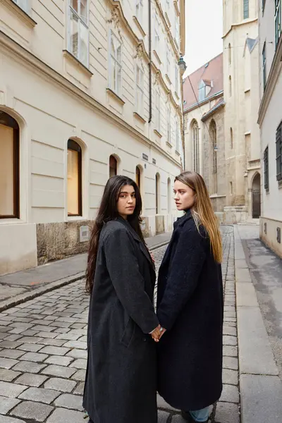 Feliz jovem casal lésbico na moda outerwear de mãos dadas enquanto caminhava na cidade europeia, lgbt — Fotografia de Stock