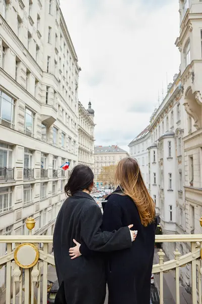 Intimate moment on balcony with city view as backdrop, back view of lesbian women in love — Stock Photo