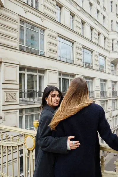 Momento íntimo en balcón con vista a la arquitectura de la ciudad como telón de fondo, jóvenes lesbianas enamoradas - foto de stock
