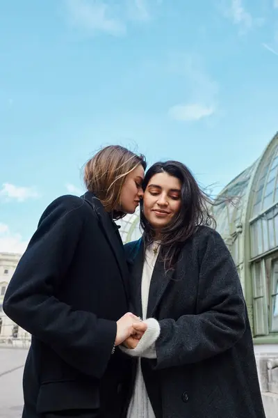 Loving lgbt couple in coats holding hands while standing near Palmenhaus in Vienna on background — Stock Photo