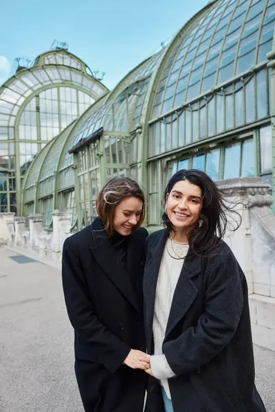 Lgbt casal em casacos da moda preto de mãos dadas enquanto ri perto de Palmenhaus em Viena — Fotografia de Stock