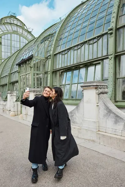 Glückliches lesbisches Paar macht Selfie auf Smartphone, während es in der Nähe des historischen Platzes in Wien steht — Stockfoto