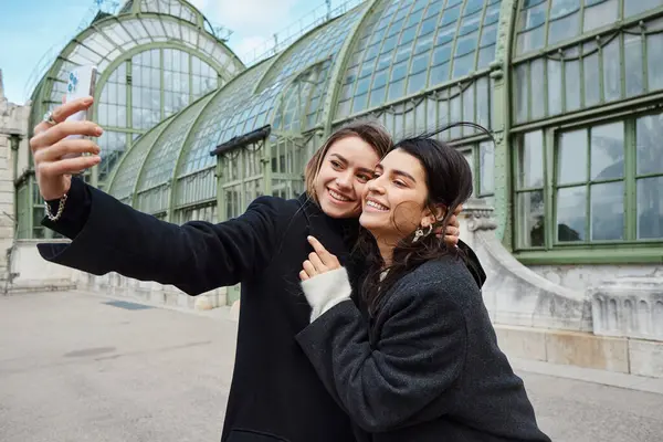 Glückliches lesbisches Paar macht Selfie auf Smartphone, während es in der Nähe des historischen Platzes in Wien steht — Stockfoto