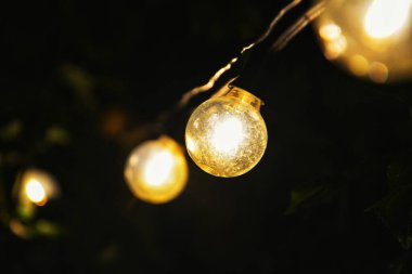 Karanlık, romantik gece aydınlatma konseptinde parıldayan sıcak bahçe ampullerinin makro çekimi.
