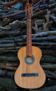 Ahşap kütüklerin önünde Rustik gitar. Dışarıdaki odun yığınına dayanmış yıpranmış akustik bir gitar. Kırsal yaşam tarzı görseller, açık hava müzik temaları ya da öykü anlatımı için ideal