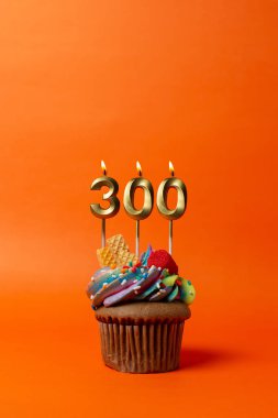 300 numaralı doğum günü pastası turuncu arka planda kek ve doğum günü mumları.