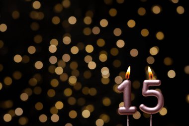 Odaklanamayan ışıklarla arka planı gösteren güzel bir görüntü bir bokeh etkisi yaratarak neşeli ve neşeli bir atmosfer yaratıyor. Bir köşede, iki tane yanan doğum günü mumu biraz sıcaklık ve kutlama katar, özel bir şeyi temsil etmek için mükemmeldir.