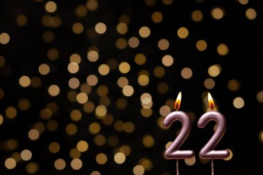 Odaklanamayan ışıklarla arka planı gösteren güzel bir görüntü bir bokeh etkisi yaratarak neşeli ve neşeli bir atmosfer yaratıyor. Bir köşede, iki tane yanan doğum günü mumu biraz sıcaklık ve kutlama katar, özel bir şeyi temsil etmek için mükemmeldir.